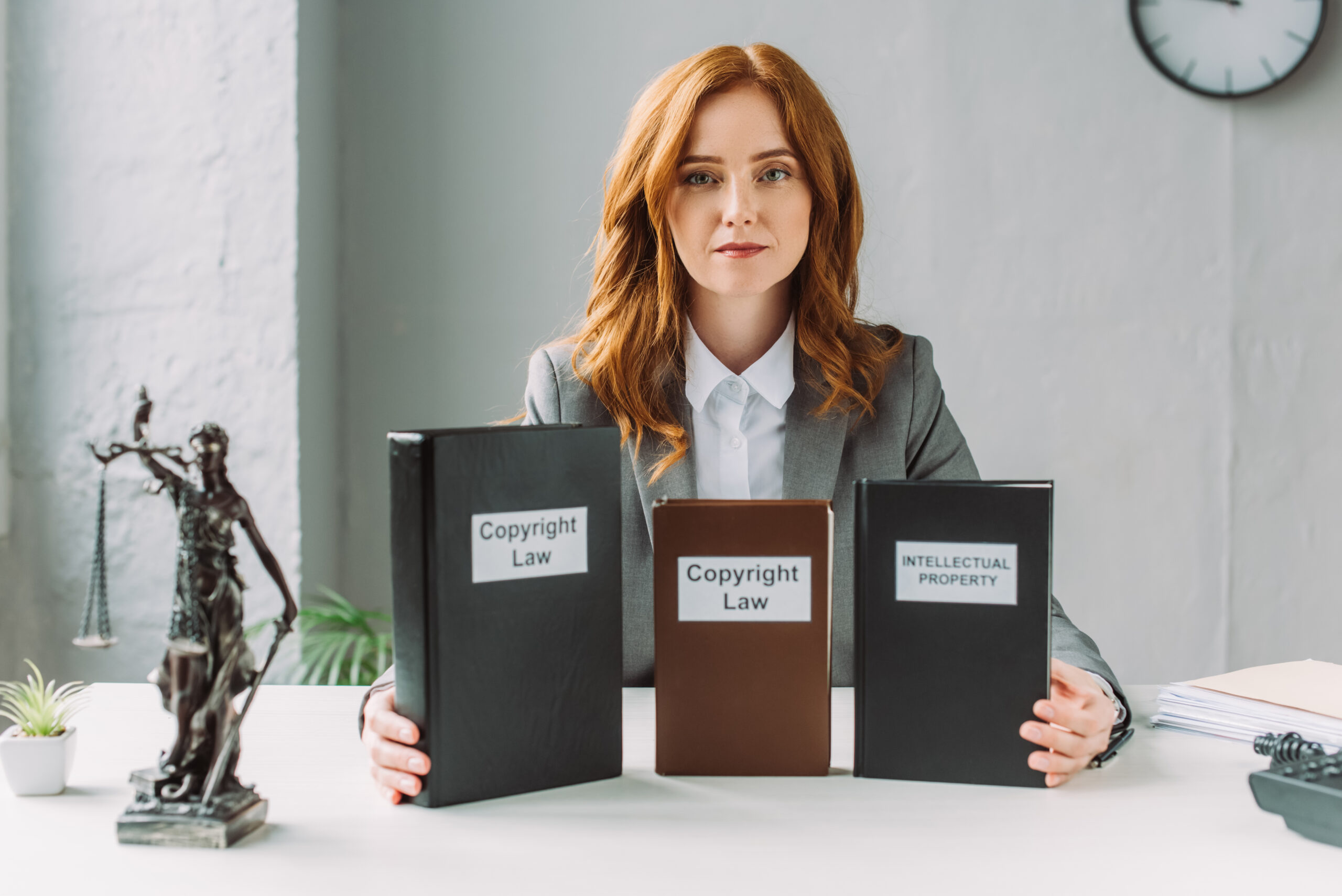 lawyer looking at camera and holding books with copyright law and intellectual property lettering, while sitting at table