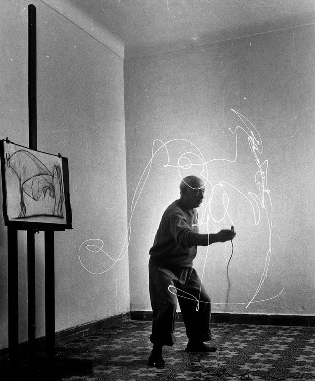 Black-and-white photograph of Pablo Picasso drawing with a small light source during a long exposure while creating light painting images