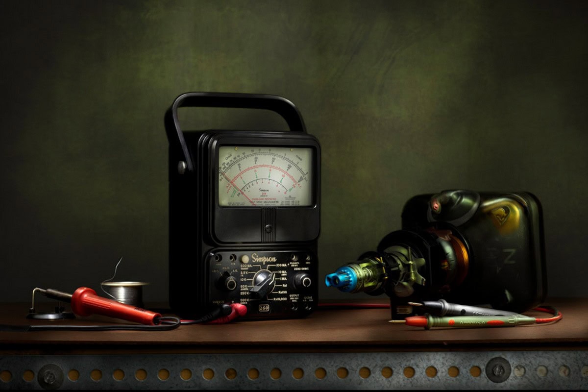 End of an Era: a vintage analog meter and a cathode ray tube on a wooden shelf, lit by hand against a dark green background.