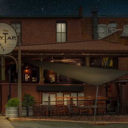 The City Tap Bar is closed for the night, the tables and chairs are empty, and the stars are out. “The City Tap Bar nightscape in Pittsboro, North Carolina illuminated by warm lamplight.”